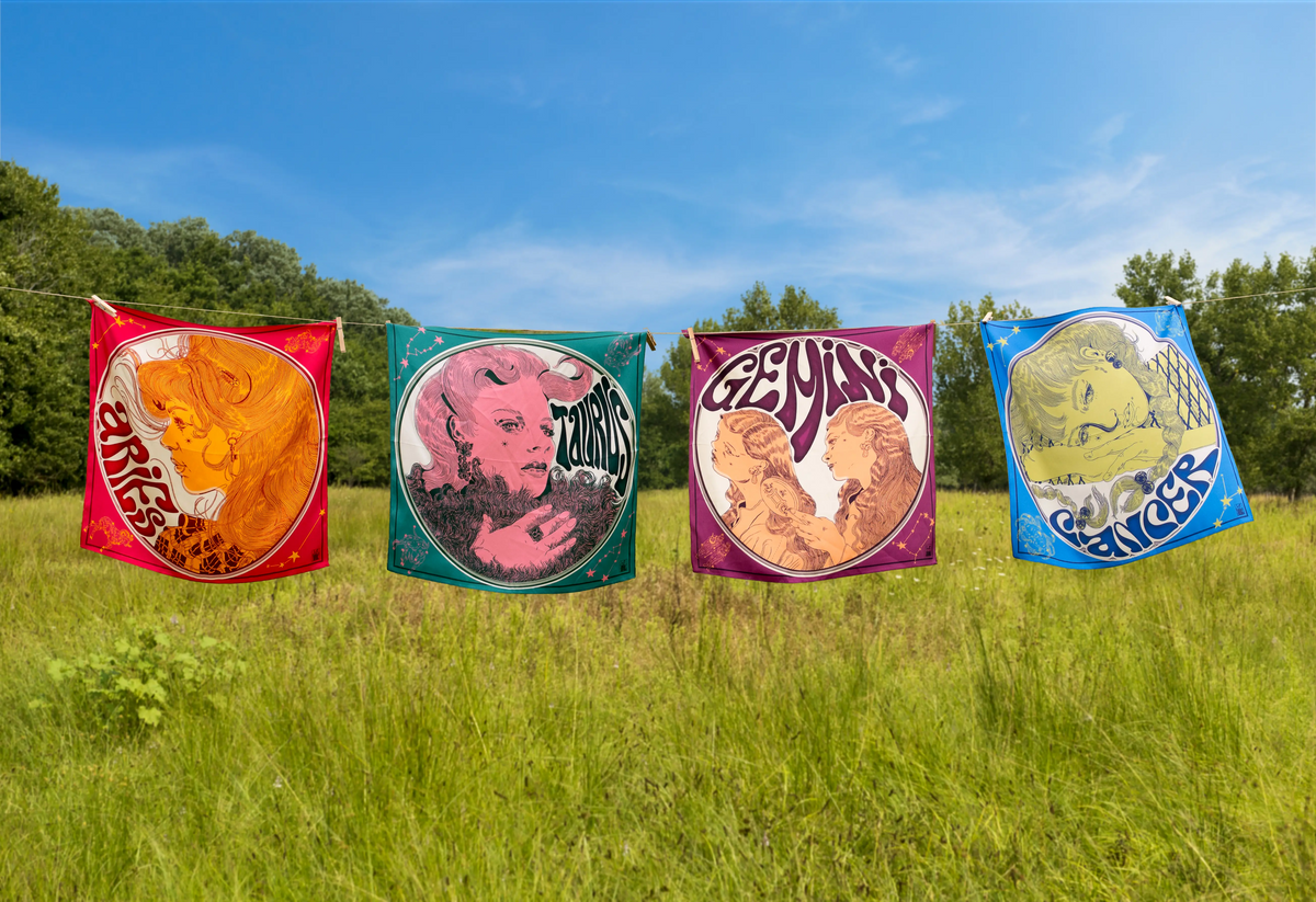 Aries, Taurus, Gemini, and Cancer zodiac scarves hanging on a clothesline outdoors.